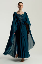 Rhea teal cape sleeve maxi dress with silver-embellished bodice, flowing cape overlay, and modest elegant silhouette for weddings and formal events.