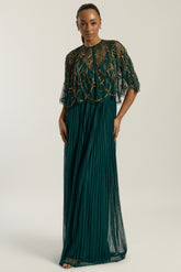 Green embellished maxi dress with flowing pleated skirt and detachable sheer cape overlay, featuring gold bead detailing and an elegant V-neck silhouette for occasion wear.