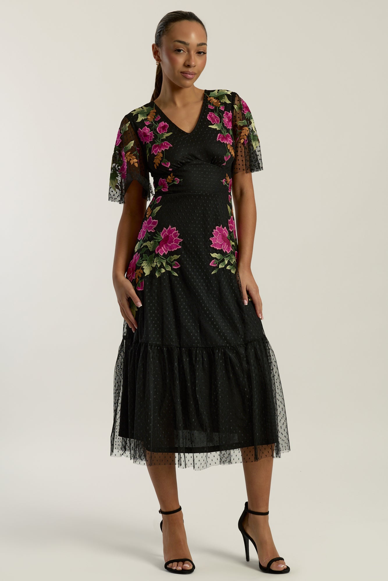 Frock and Frill Elena black midi dress with colourful floral embroidery, sheer polka dot mesh overlay, V neckline and flared sleeves.