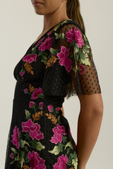 Frock and Frill Elena black midi dress with colourful floral embroidery, sheer polka dot mesh overlay, V neckline and flared sleeves.