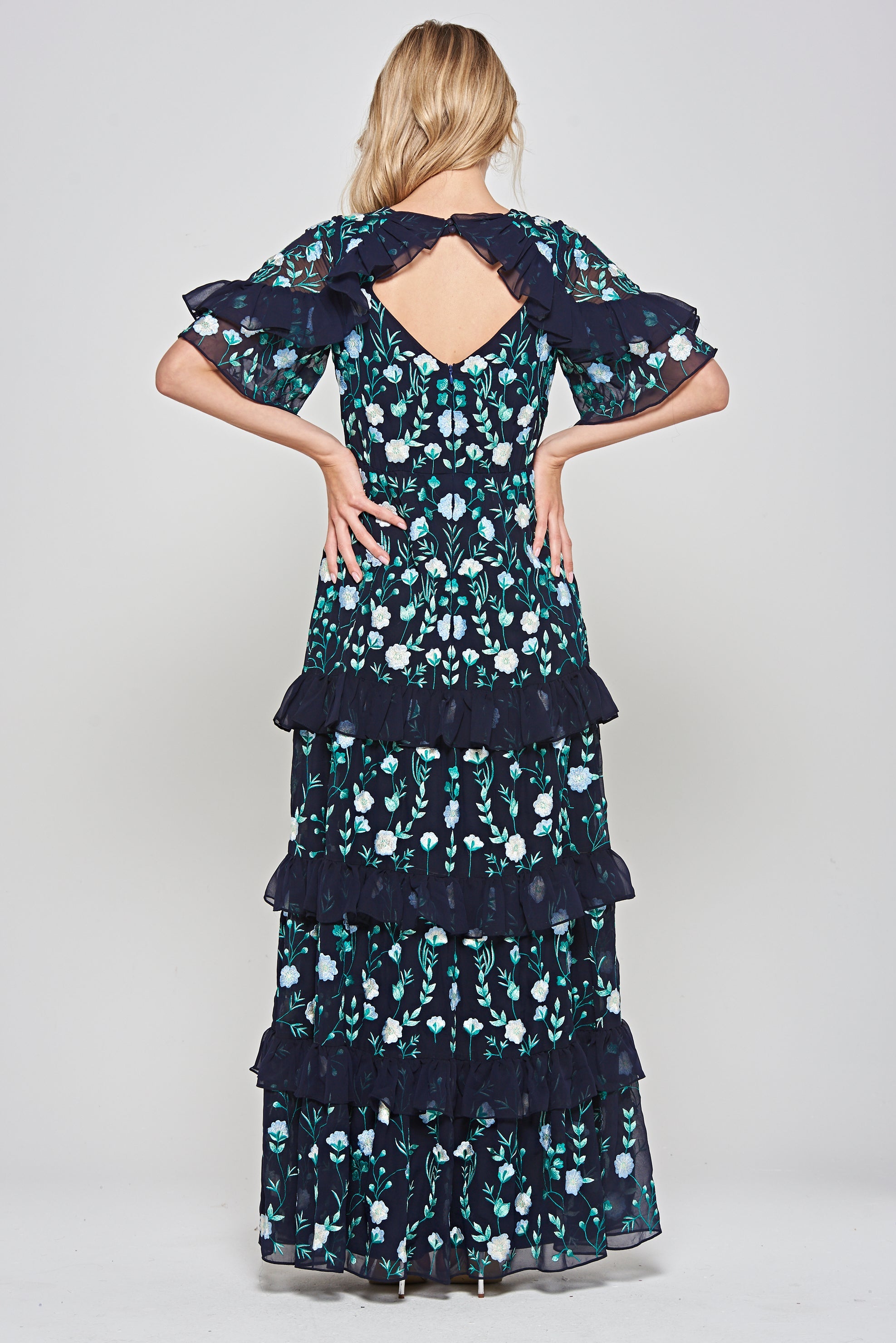 Jasmine navy maxi dress by Frock and Frill with floral embroidery, ruffled tiered skirt, and sheer flutter sleeves, styled for weddings and garden parties.