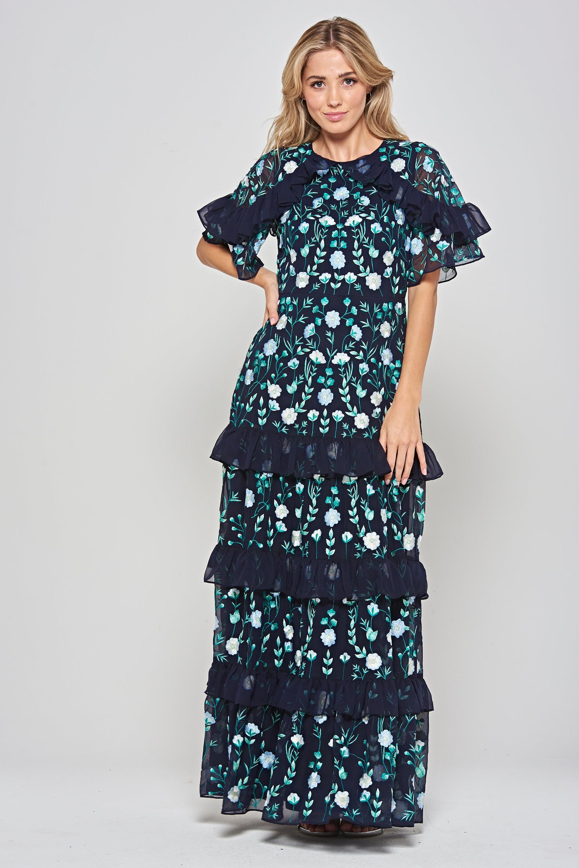 Jasmine navy maxi dress by Frock and Frill with floral embroidery, ruffled tiered skirt, and sheer flutter sleeves, styled for weddings and garden parties.