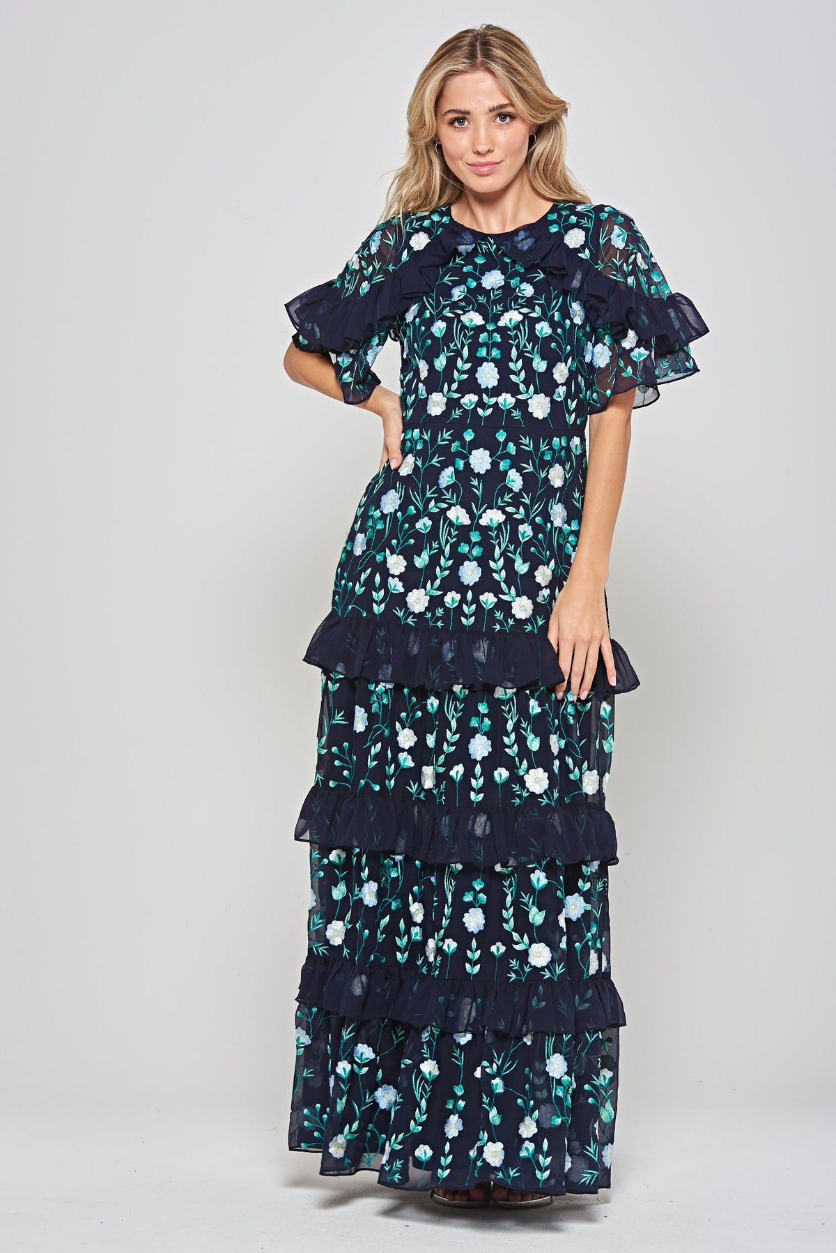 Jasmine navy maxi dress by Frock and Frill with floral embroidery, ruffled tiered skirt, and sheer flutter sleeves, styled for weddings and garden parties.