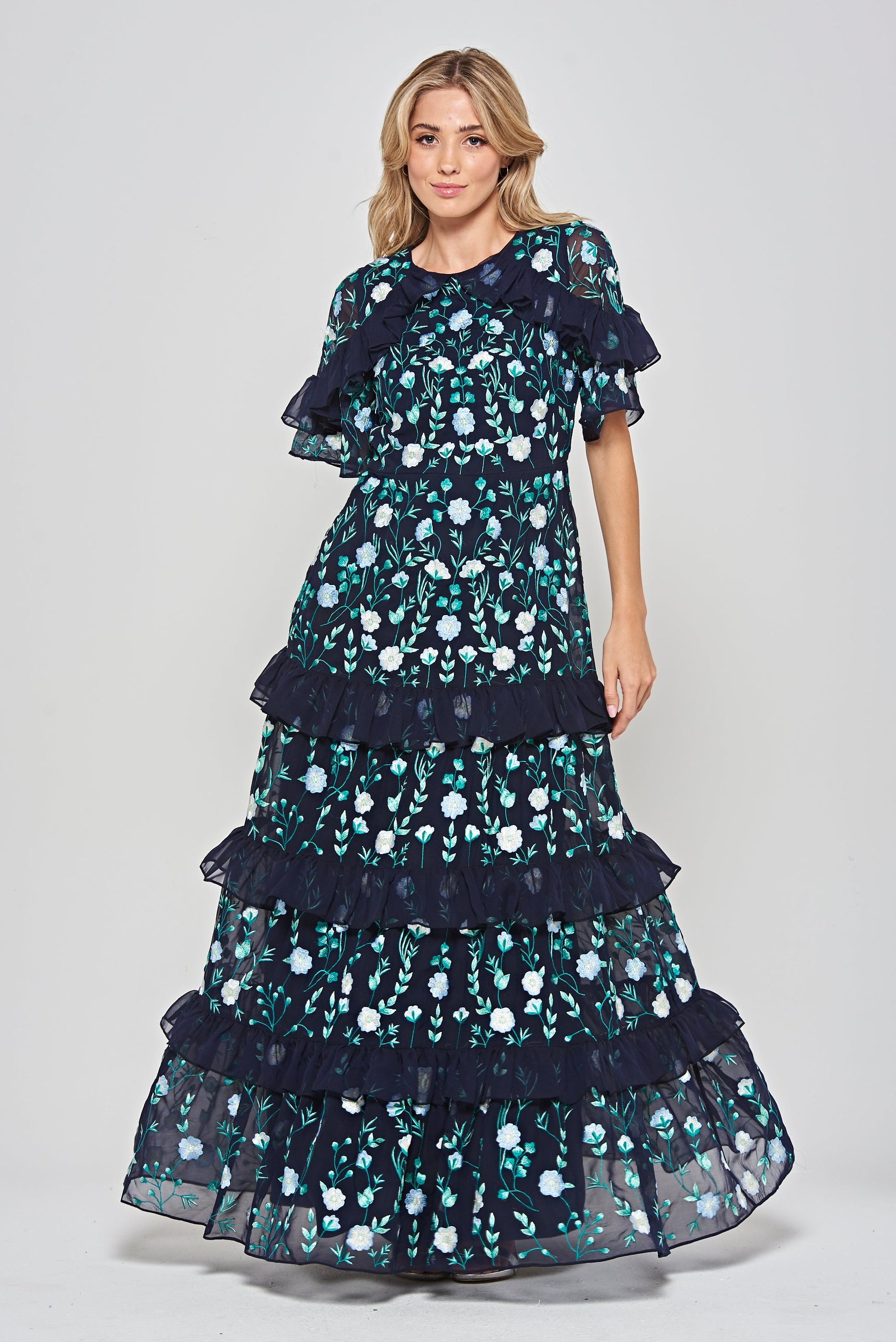 Jasmine navy maxi dress by Frock and Frill with floral embroidery, ruffled tiered skirt, and sheer flutter sleeves, styled for weddings and garden parties.