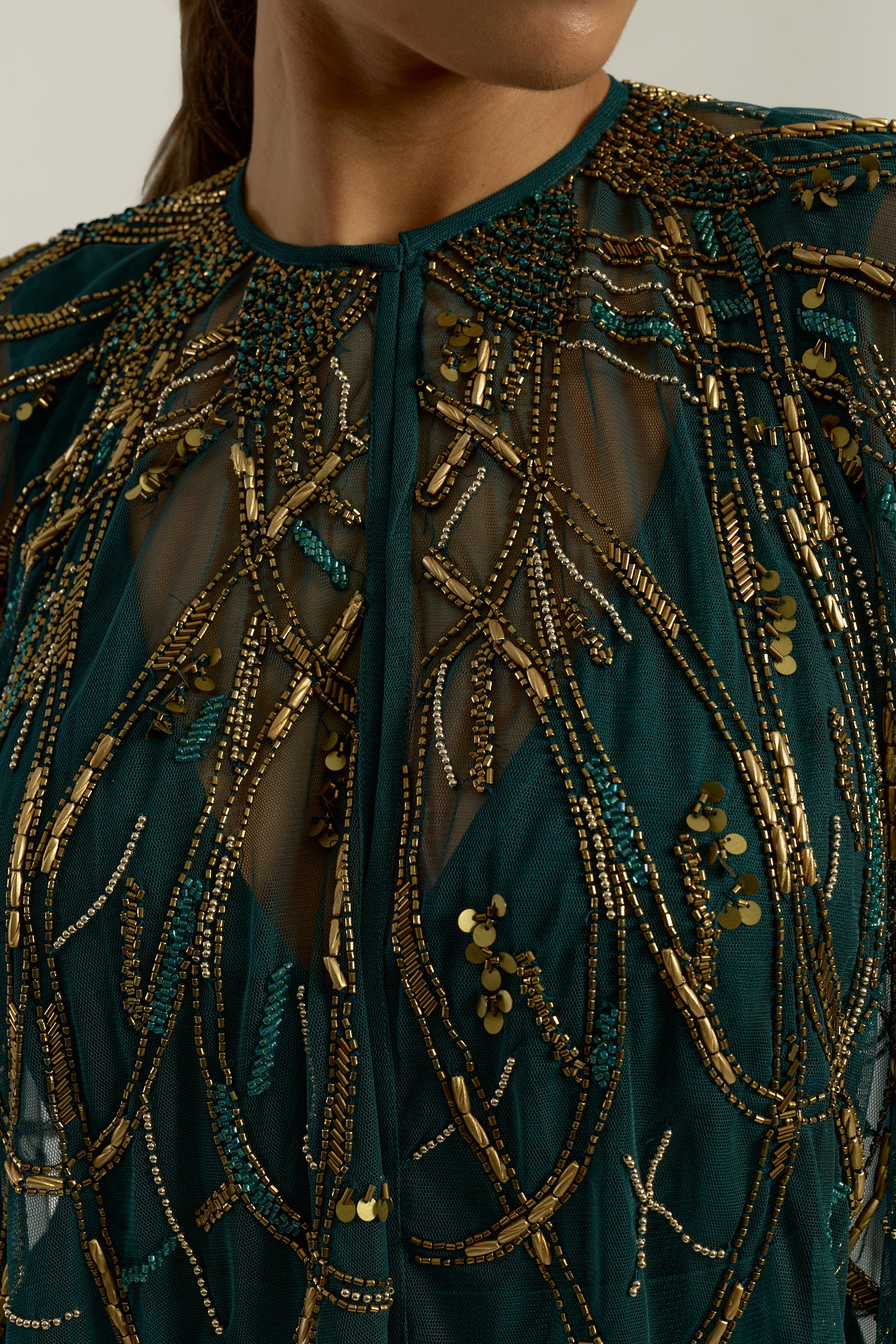 Green embellished maxi dress with flowing pleated skirt and detachable sheer cape overlay, featuring gold bead detailing and an elegant V-neck silhouette for occasion wear.