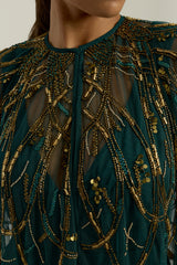 Green embellished maxi dress with flowing pleated skirt and detachable sheer cape overlay, featuring gold bead detailing and an elegant V-neck silhouette for occasion wear.