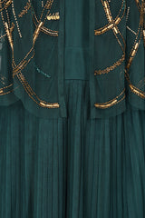 Green embellished maxi dress with flowing pleated skirt and detachable sheer cape overlay, featuring gold bead detailing and an elegant V-neck silhouette for occasion wear.